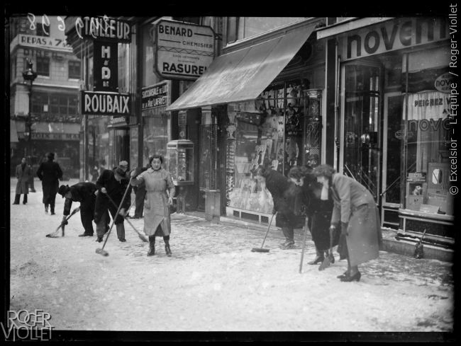 Commerçants balayant les trottoirs devant leurs boutiques sous la neige.