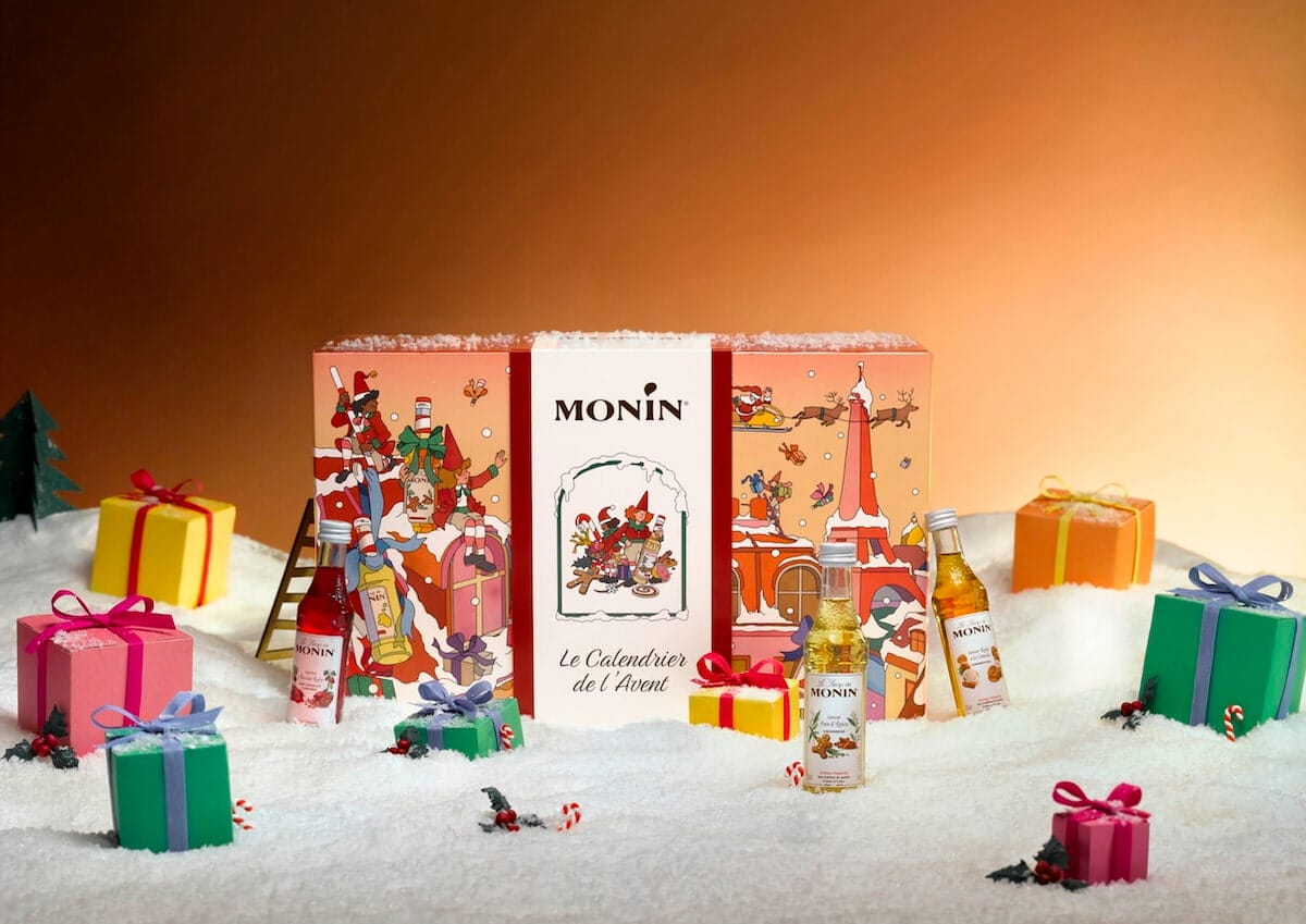 Calendrier de l'Avent Monin 2026 illustré de scènes de Noël parisiennes, entouré de petites bouteilles de sirop et de cadeaux colorés.