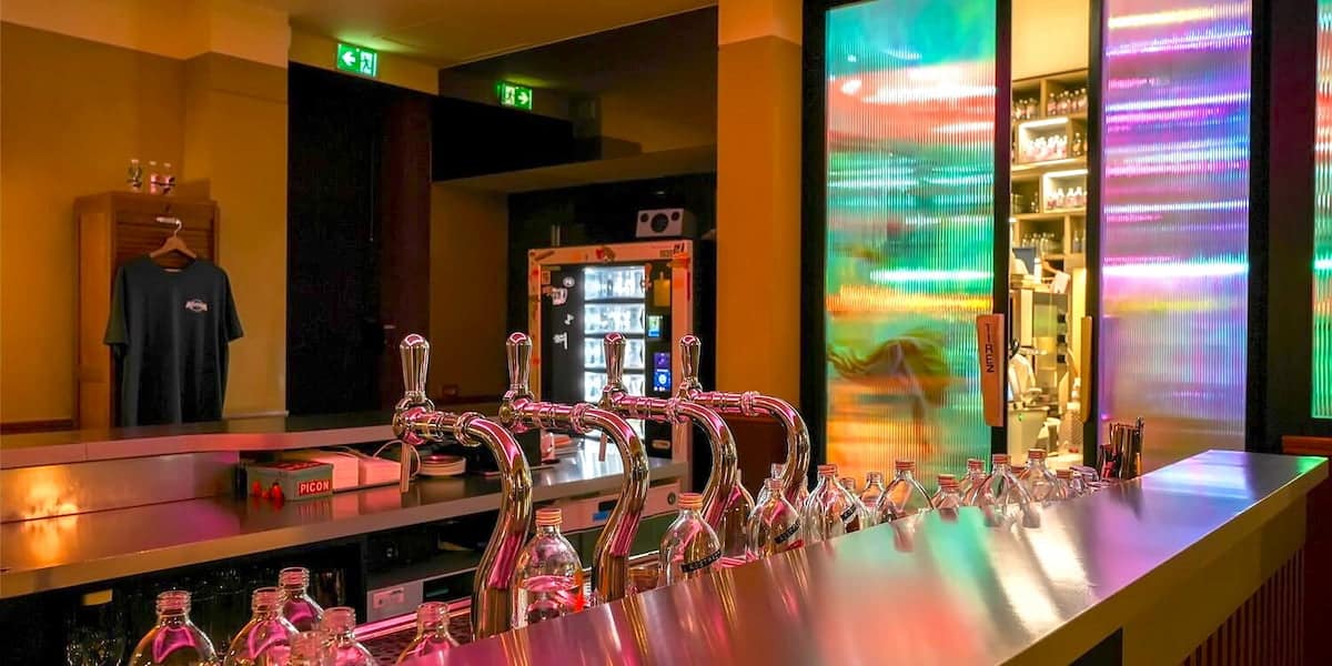 Comptoir du bar Abstract à Lyon avec les tireuses, les bouteilles et les jeux de lumière colorés
