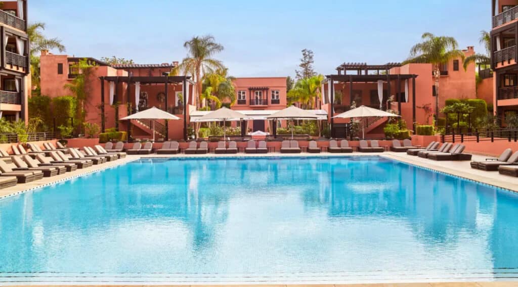 Piscine du Naoura Marrakech, hôtel Barrière situé près de la médina, avec façades ocres, transats et palmiers.