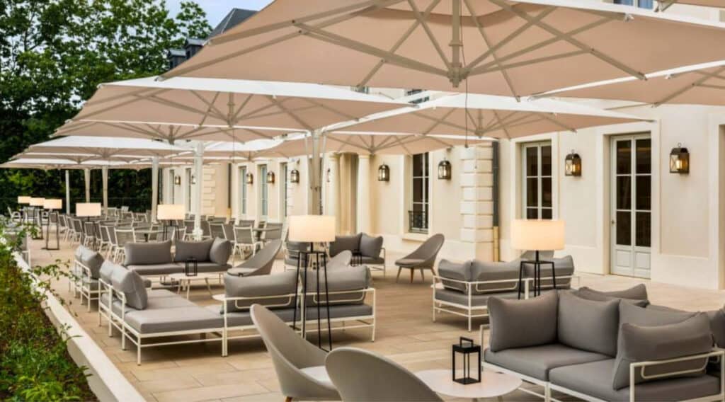 Terrasse Andy du Dolce Versailles avec parasols, salons extérieurs et tables installées dans un cadre verdoyant près de Paris