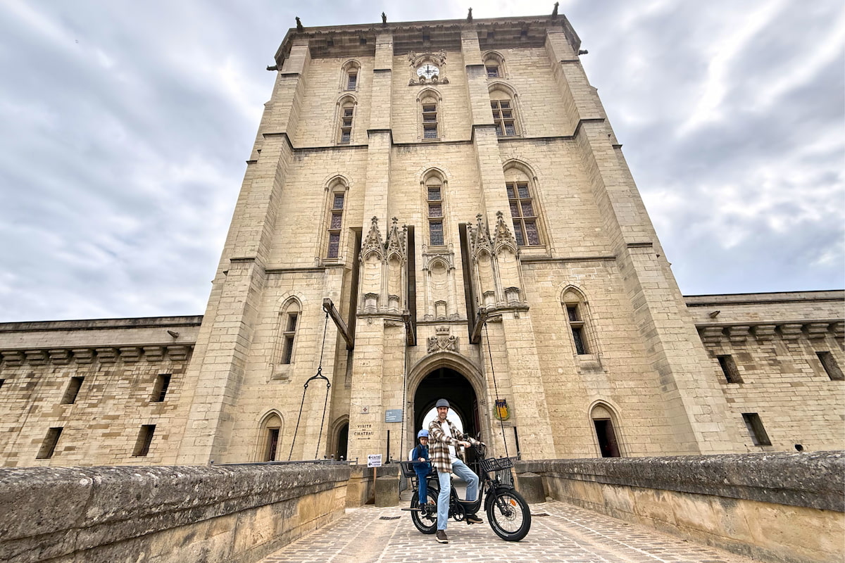 Un adulte et un enfant sur un vélo cargo Ritmic Jumbo devant l’entrée du château de Vincennes.