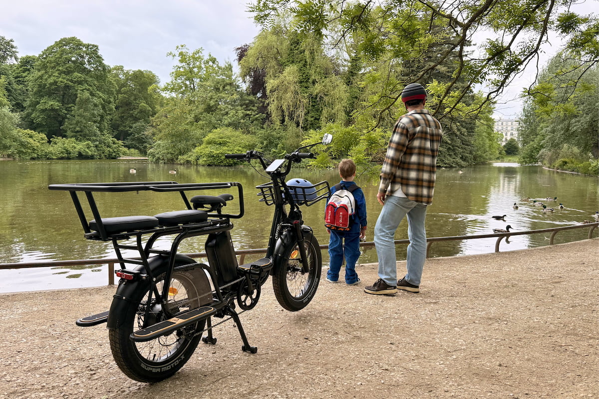 Un vélo cargo Ritmic Jumbo garé près du lac Daumesnil, avec un adulte et un enfant observant les canards au bord de l’eau.