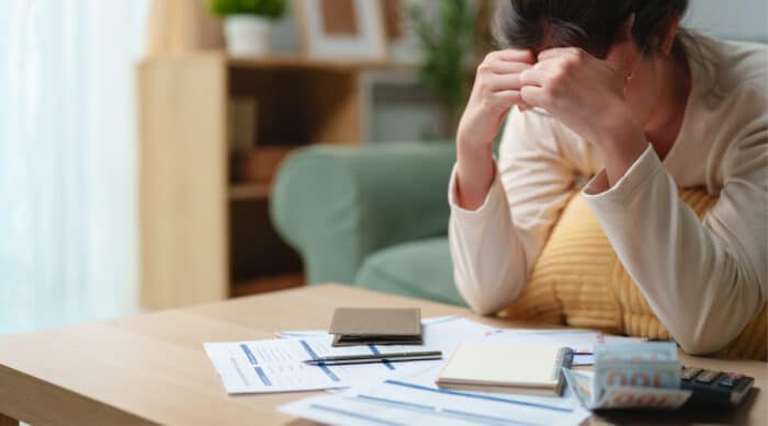 Une femme consulte ses documents financiers avec une calculatrice et un ordinateur pour gérer ses impôts et son épargne.