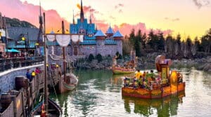Vue de Disneyland Paris au coucher du soleil avec le château et des bateaux sur le lac