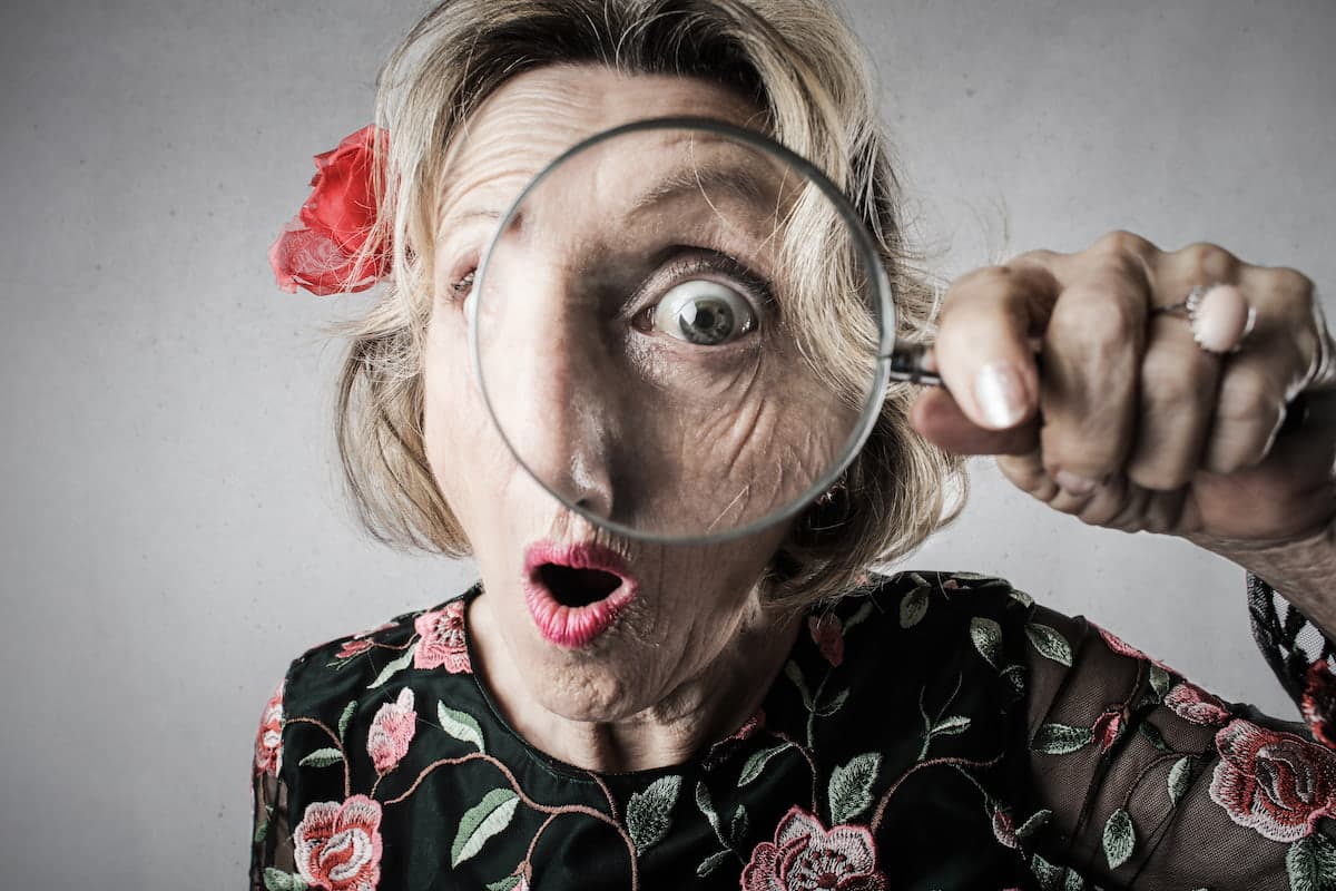 Une femme regarde à travers une loupe avec une expression surprise.