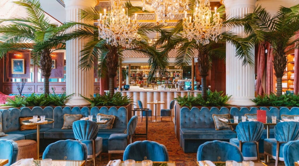 Intérieur du Café Lapérouse à La Vallée Village avec ses banquettes bleues, ses palmiers et ses lustres en cristal