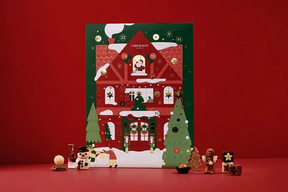 Calendrier de l'Avent Sélection 2026 de Läderach, en forme de maison de Noël rouge et verte, entouré de chocolats.